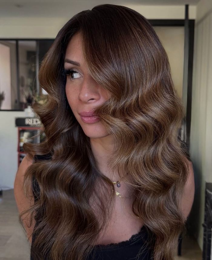 Longs cheveux châtains ondulés, balayage doré, coiffés au salon.