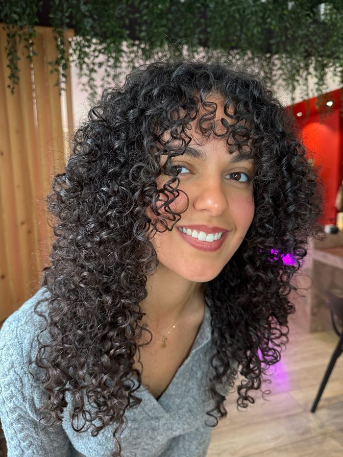 Boucles brunes volumineuses et frange bouclée, coiffées au salon.